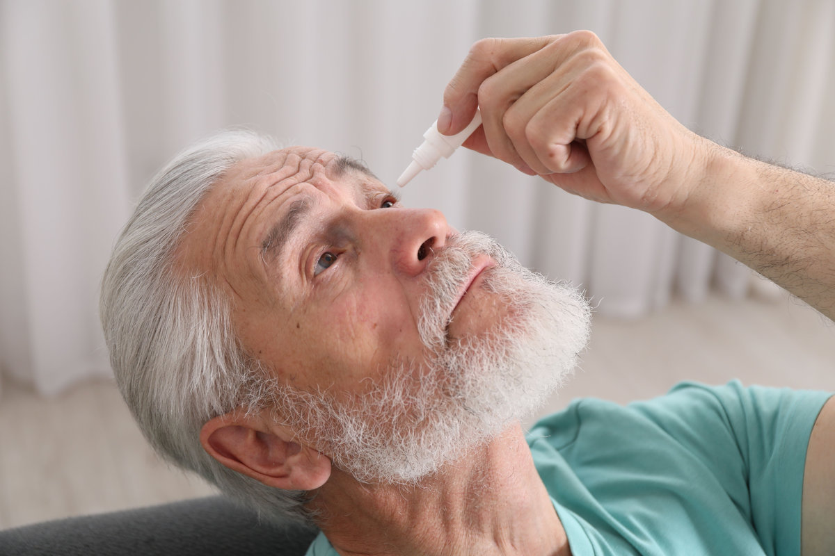Senior man applying eye drops at home