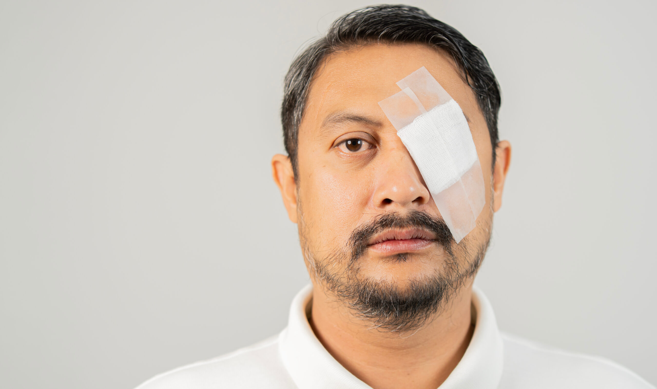 Portrait of a adult Asain man has an eye injury, putting a bandage on it, standing on white background with copy space. Close-up.