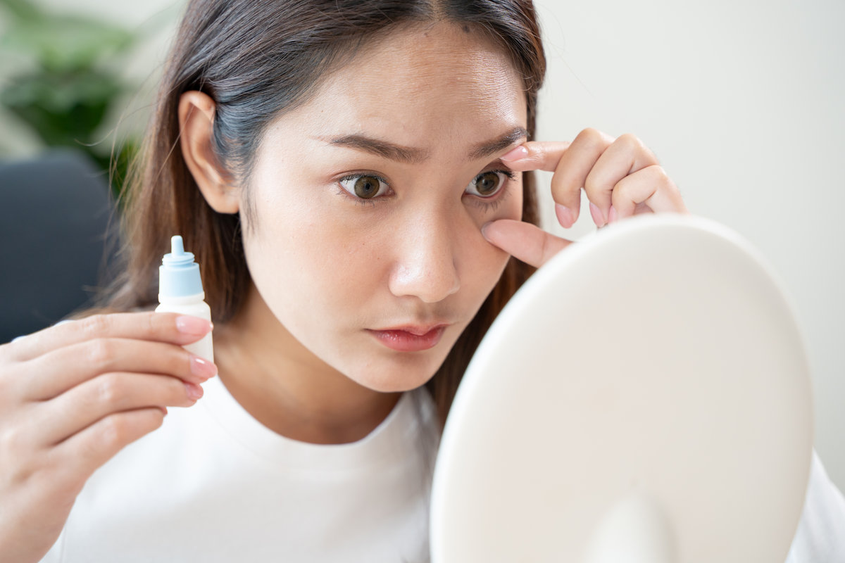 asian young woman using medical eye drops to treat dry eye and irritation.