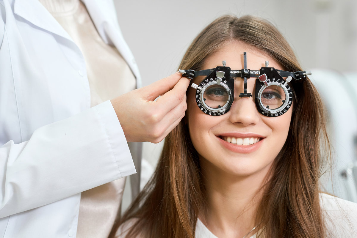 Young pretty patient wearing visual inspection device during admission to an ophthalmologist. Health saving, vision imroving. Feeling satisfied. Doctor is giving advices.