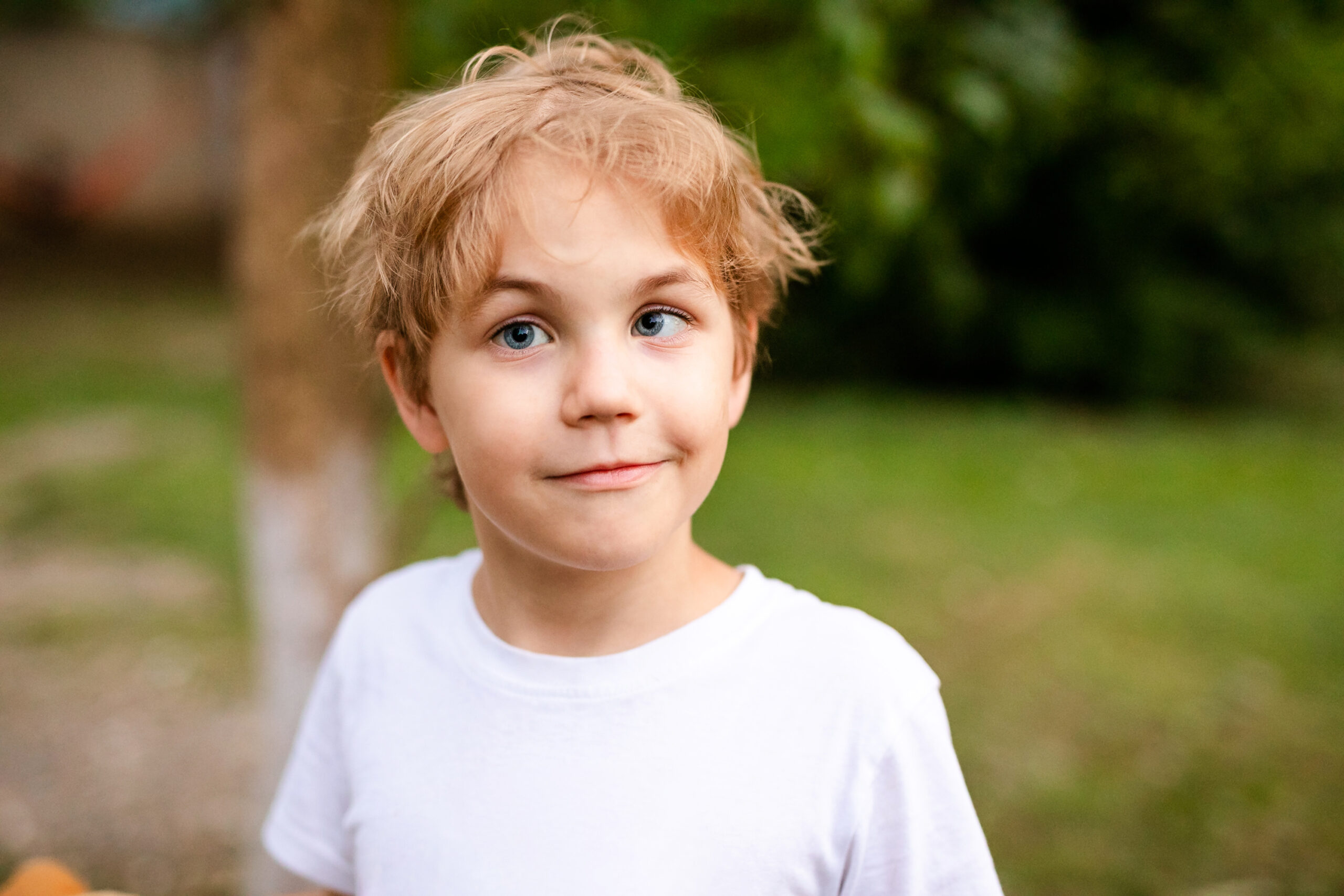 Blonde smiling boy with strabismus in warm park.