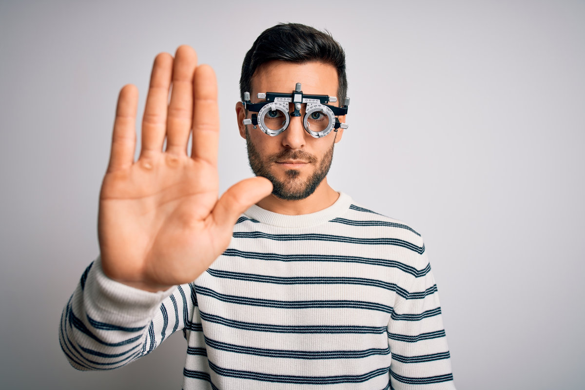 Young handsome man with beard wearing optometry glasses over isolated white background doing stop sing with palm of the hand. Warning expression with negative and serious gesture on the face.