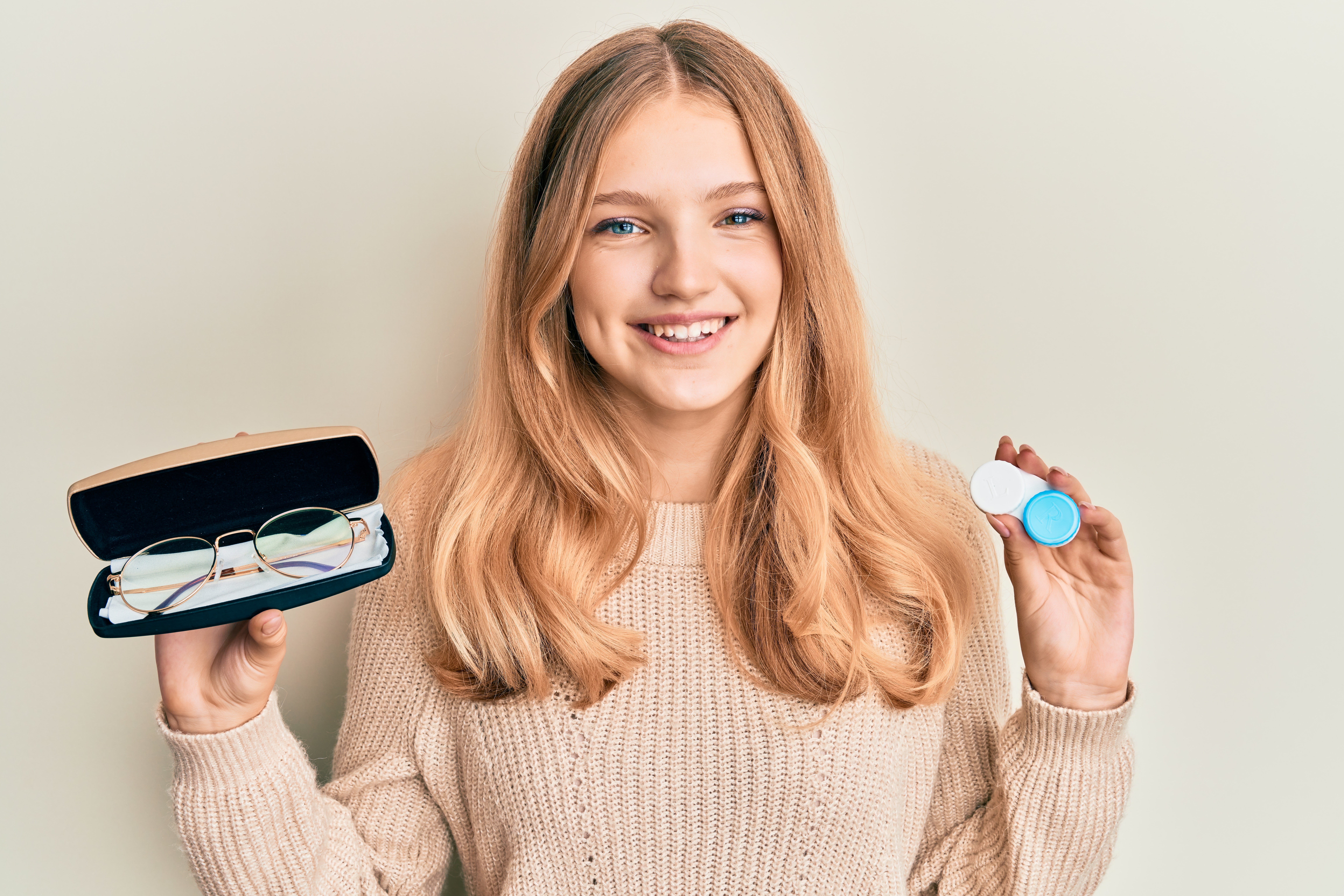Beautiful young caucasian girl holding glasses and contact lenses smiling with a happy and cool smile on face. showing teeth.
