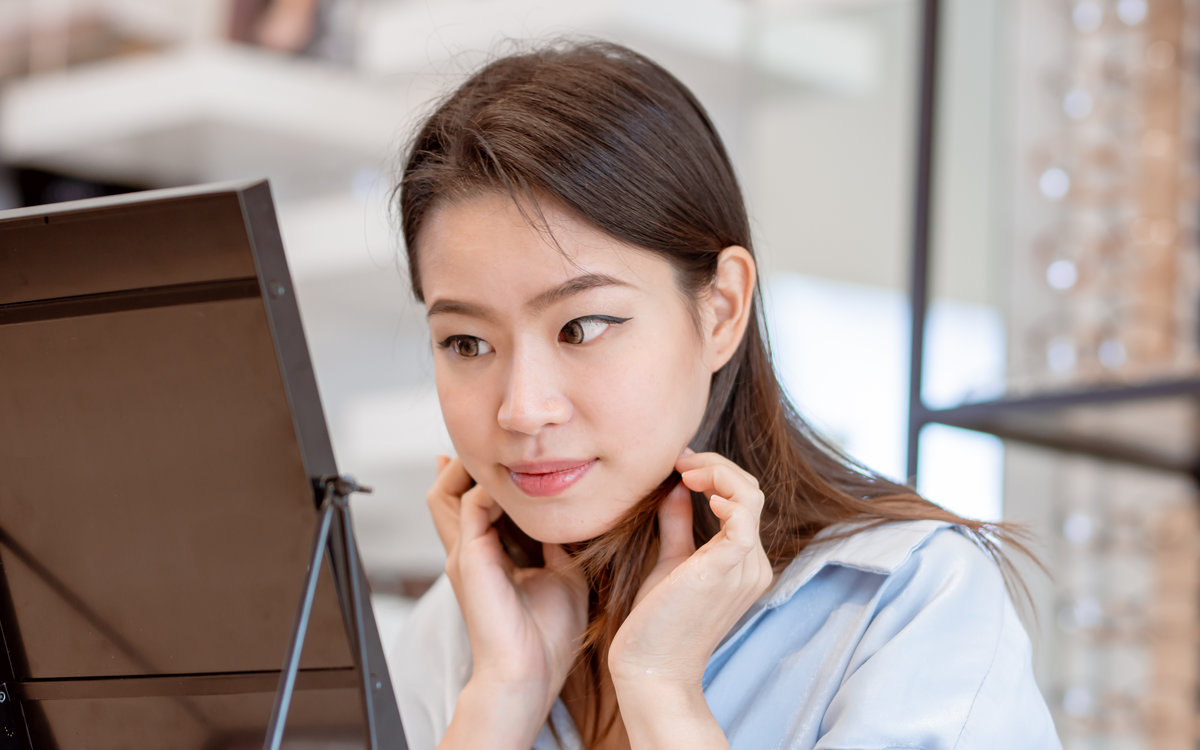 Asian beautiful woman trying to put contact lenses into her eyes and looking to the mirror. Lifestyle and Optic Concept.