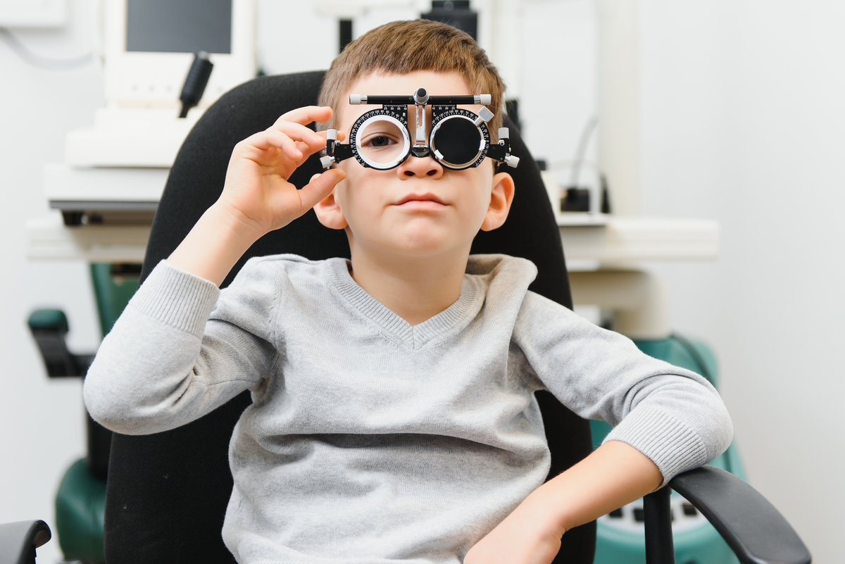 Cheerful child boy in glasses checks eye vision pediatric ophthalmologist.