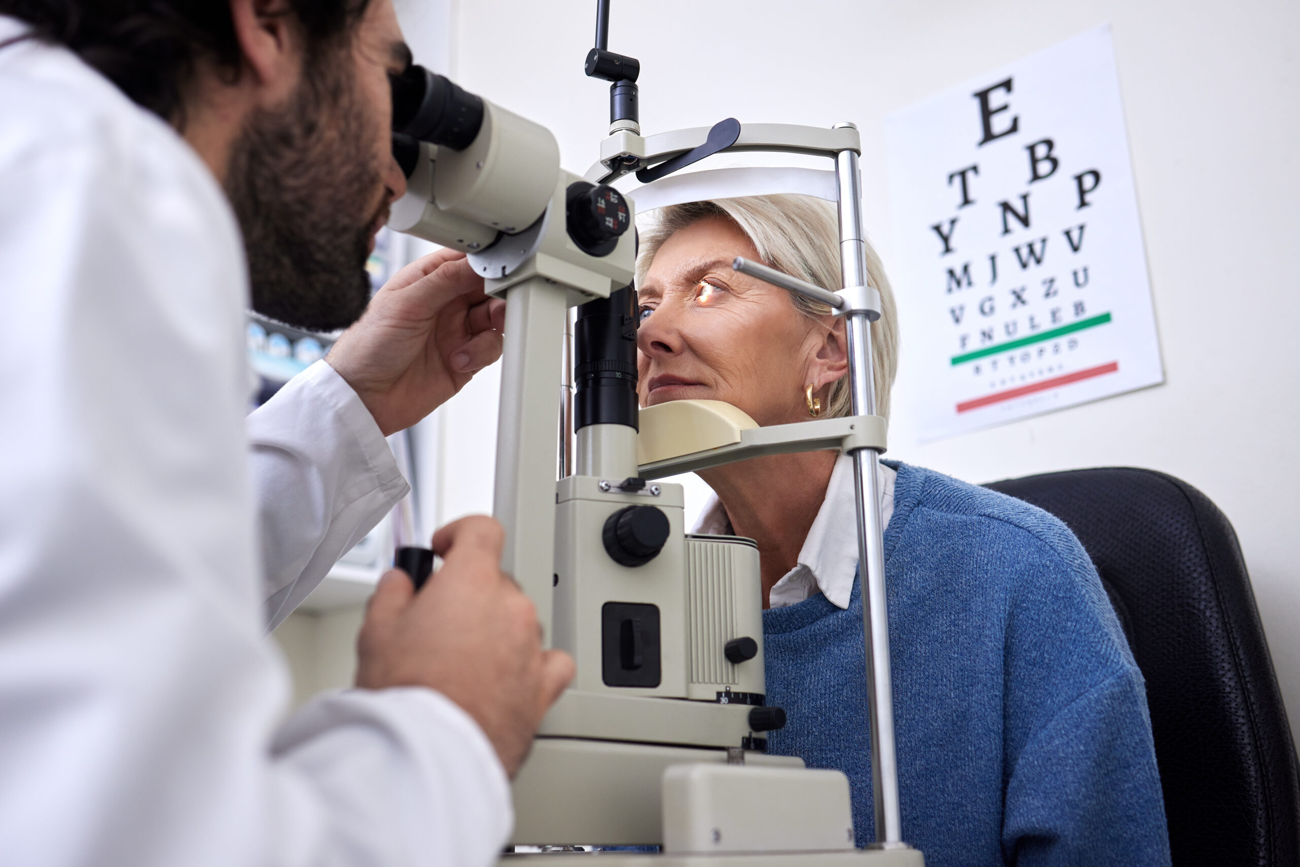 Vision, machine exam and woman with an optometrist for a check, eye consultation and lens test. Healthcare, help and male optician with a senior patient to measure visual eyesight with equipment.
