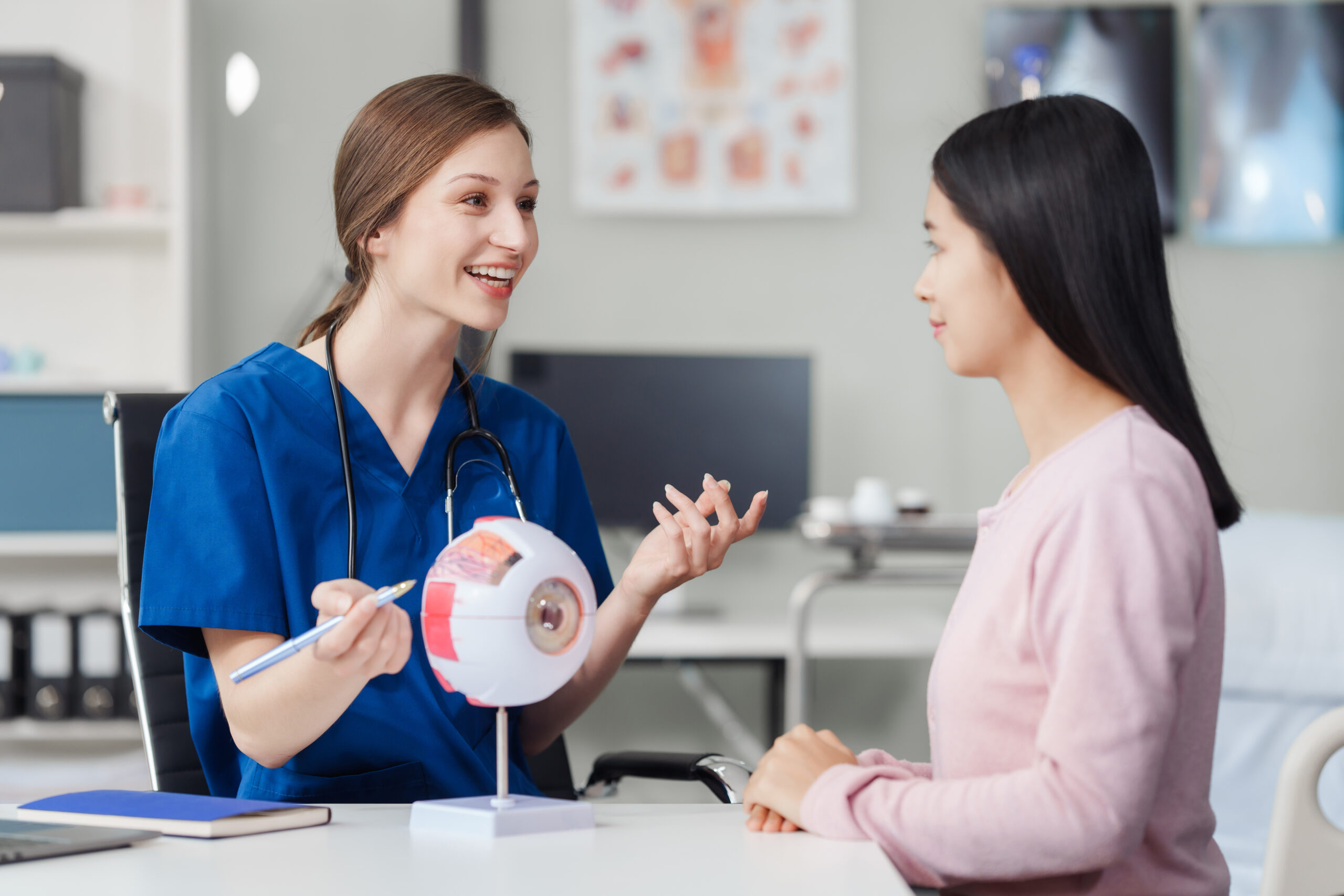 Female Caucasian ophthalmologist explains about eye diseases using the eye model with an Asian female patient At the table in the hospital examination room, Glaucoma, Cataract, Diabetic Retinopathy