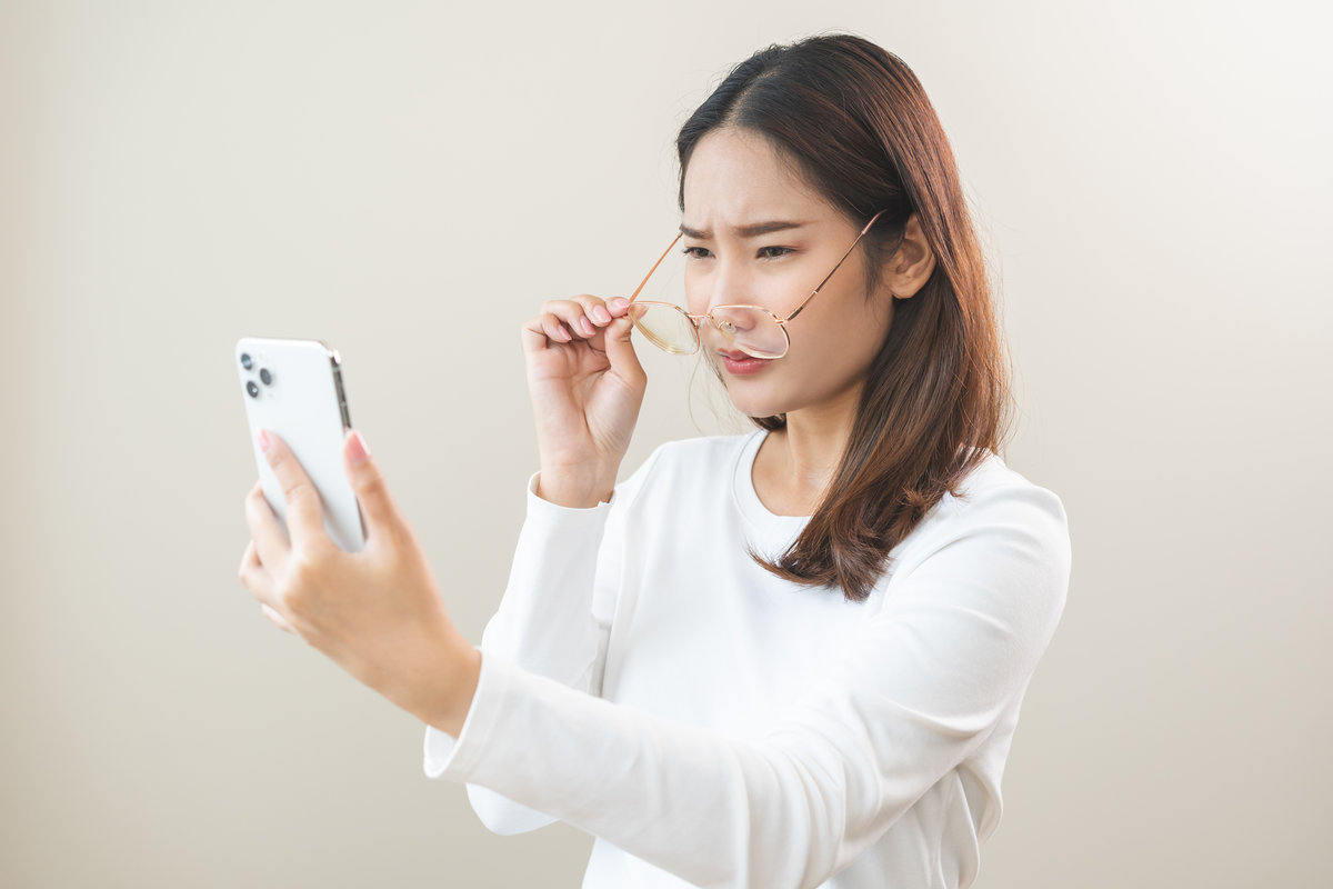 Presbyopia, Hyperopia middle aged asian woman holding eyeglasses problem with vision blurred ,trying to read text message from smart mobile phone screen, eye disease of old, eyesight farsightedness.