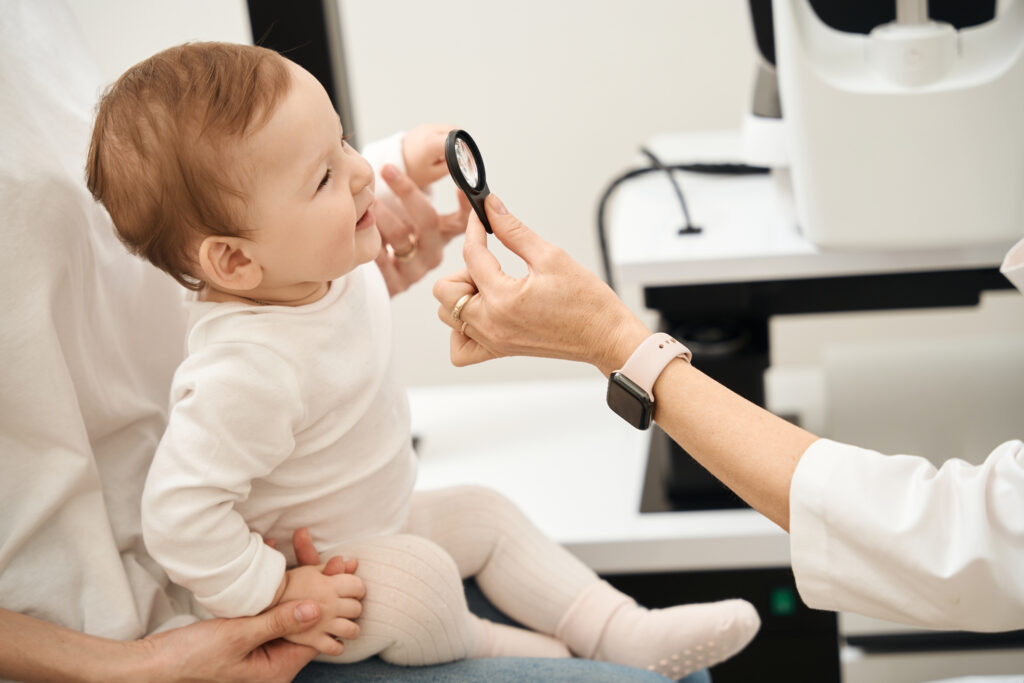 Ophthalmologist hand holding loupe in front of baby face in parent presence