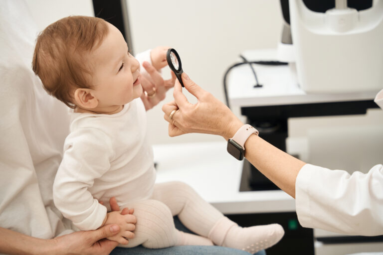 Ophthalmologist hand holding loupe in front of baby face in parent presence