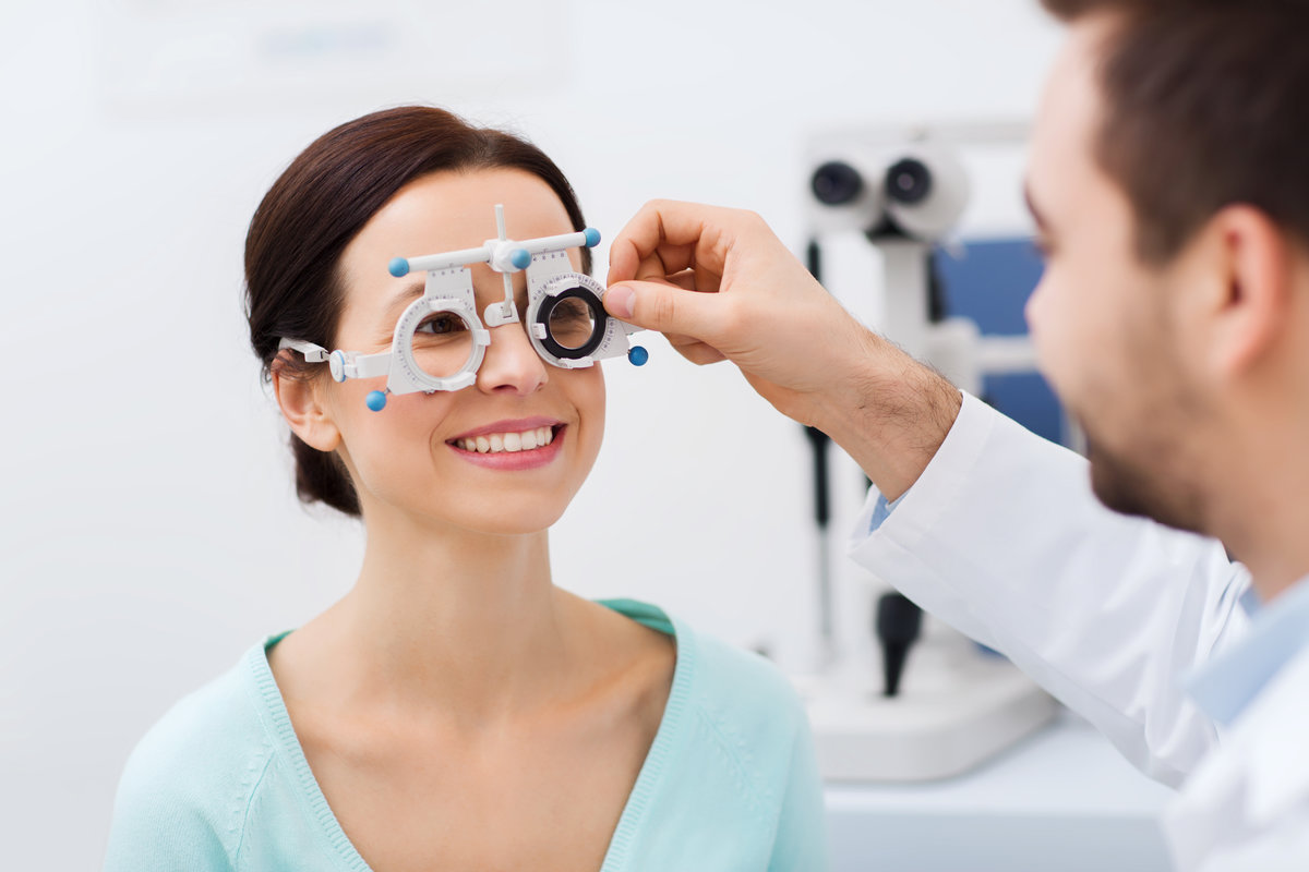 health care, medicine, people, eyesight and technology concept - optometrist with trial frame checking patient vision at eye clinic or optics store