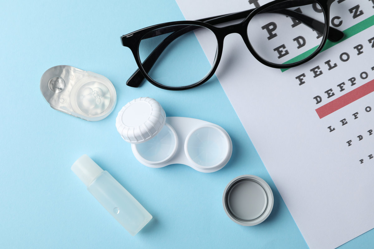 Glasses, contact lenses and eye test chart on blue background, top view