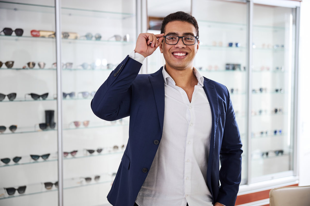 Front view of a smiling cute male buyer trying new spectacles in an optical shop
