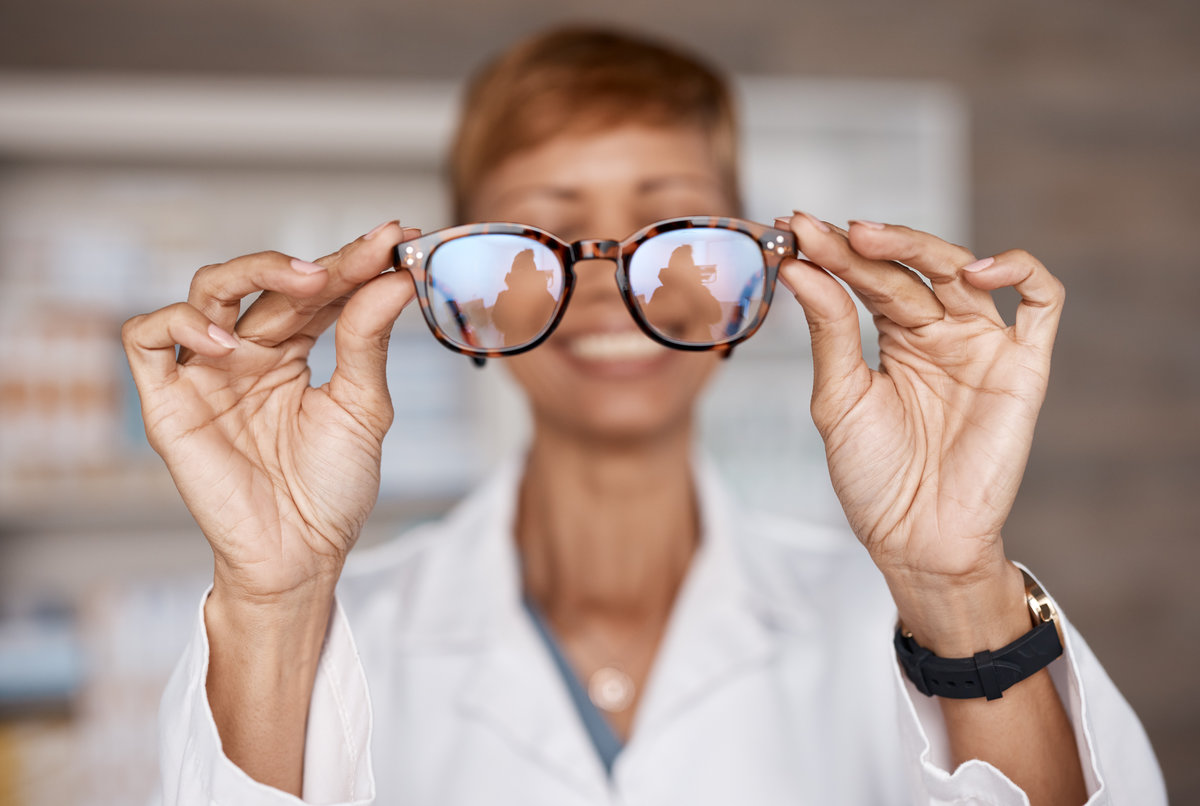 Optometry, hands and doctor with glasses in hospital or clinic for ophthalmology. Vision, healthcare and happy woman or medical optician with spectacles, frames or lenses for eye care and wellness.
