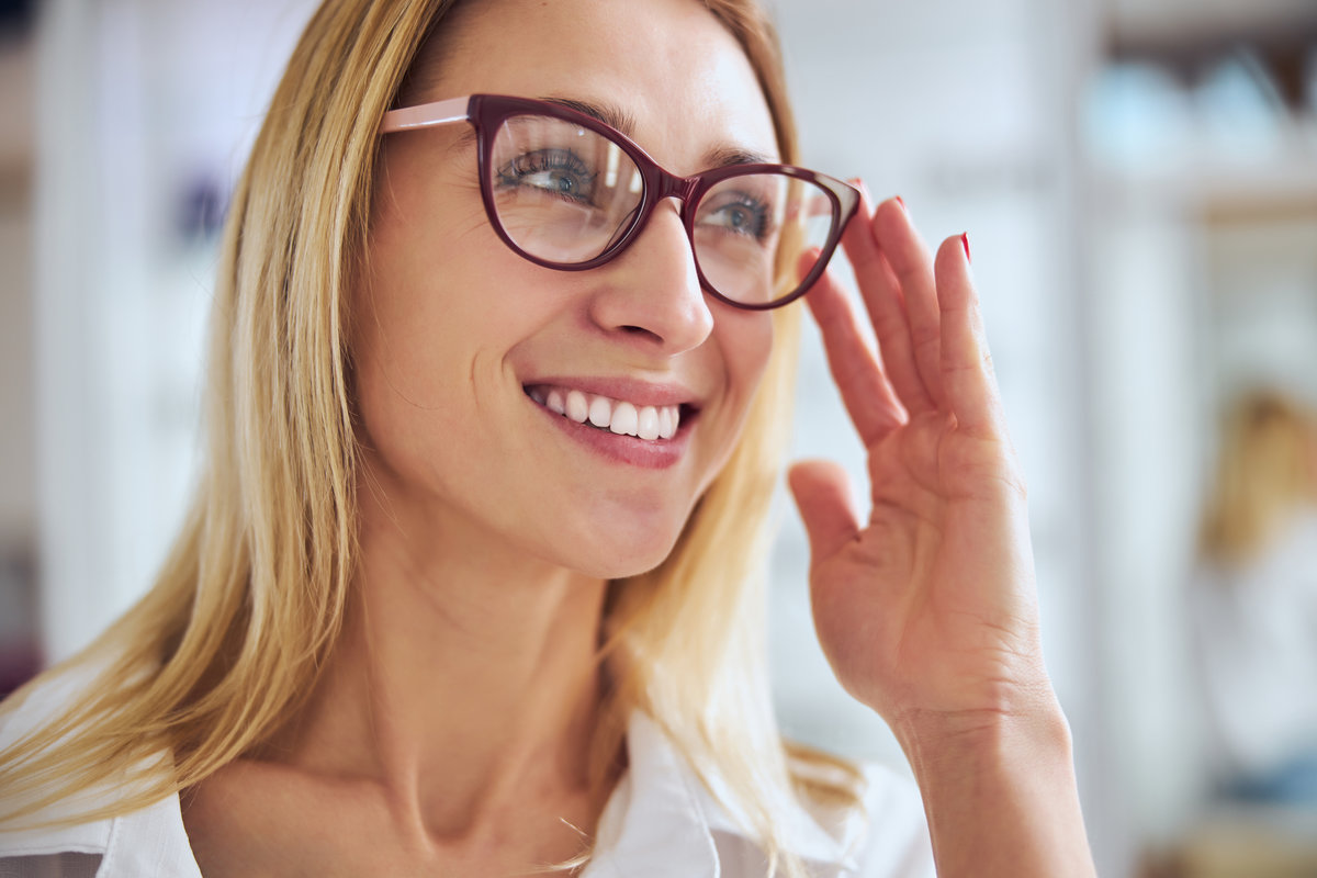 Close up portrait of good looking stylish woman in white shirt holding hand near eyeglasses in room indoors
