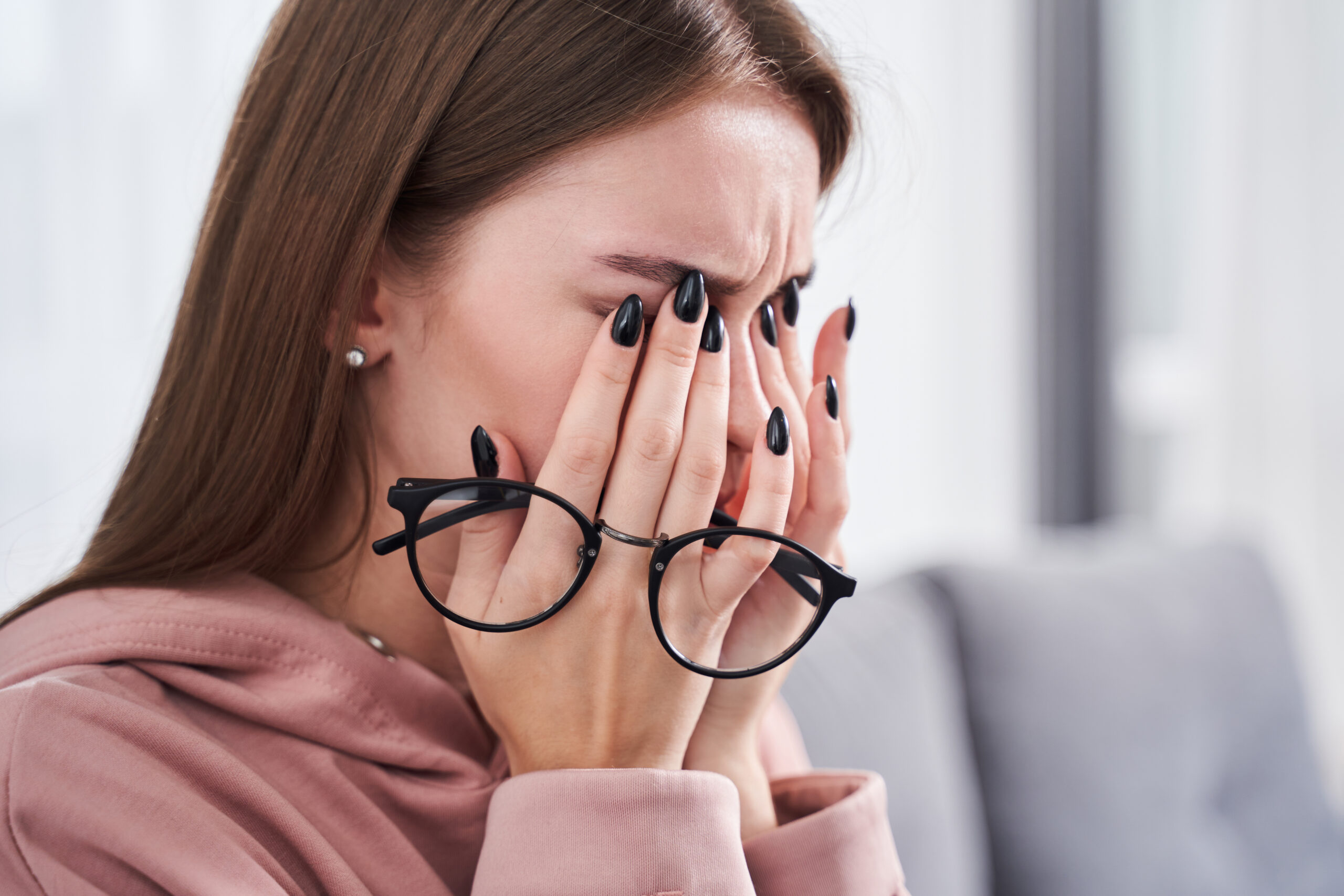Portrait view of tired young woman feeling pain eyestrain and rubbing dry irritated eyes while sitting at the sofa after hardworking with her laptop. Stock photo