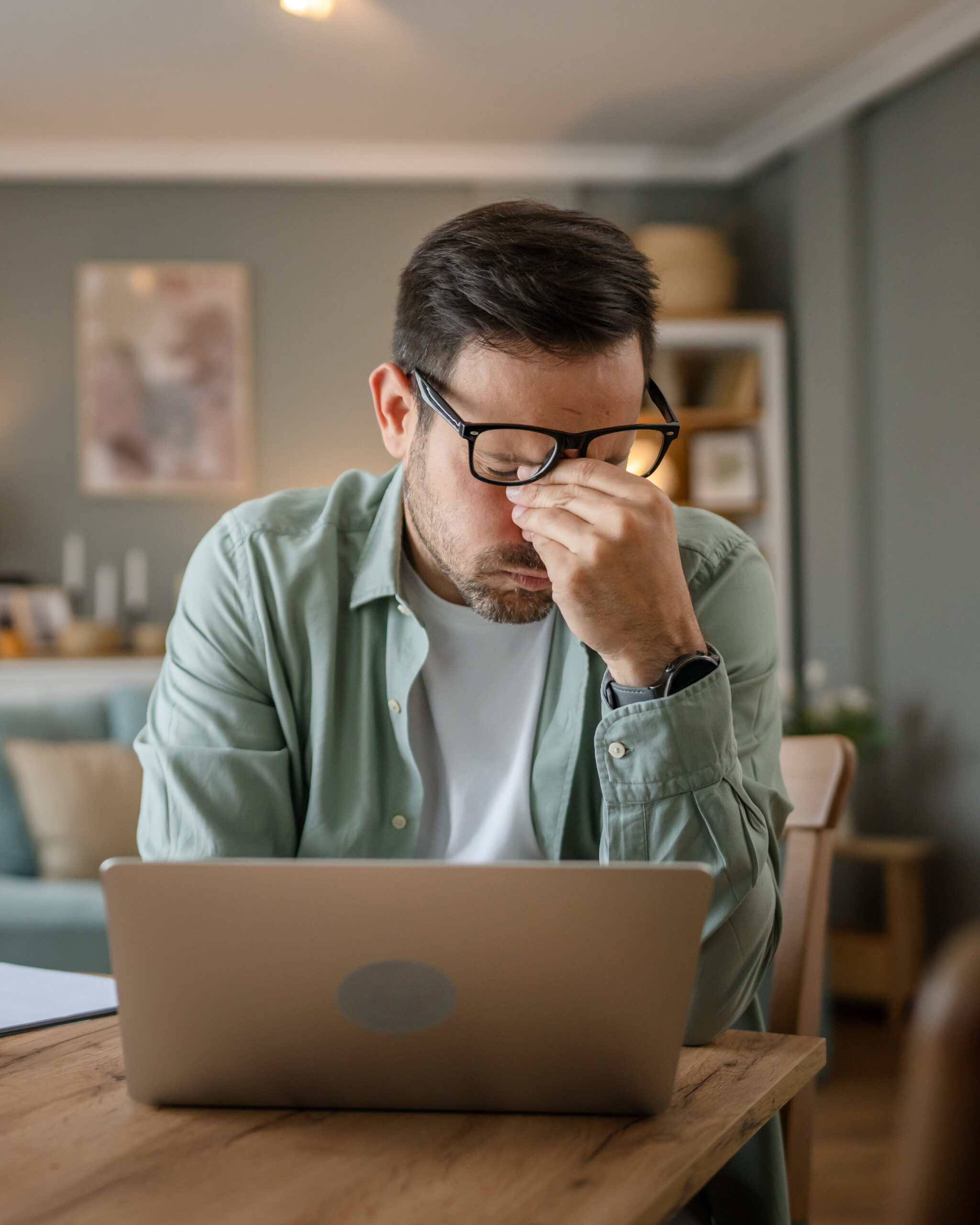 One man sitting at the desk at work in chair tired overworked and exhausted having eyestrain due long usage of laptop computer hold eyeglasses real people freelancer eye pain hold head