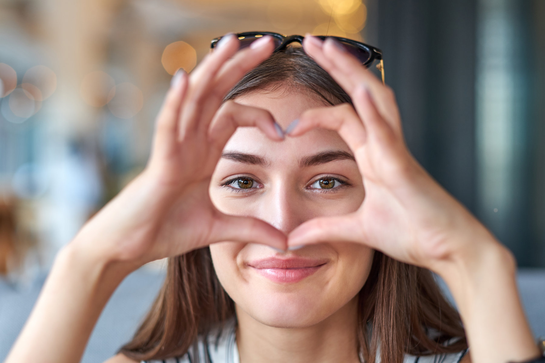 Beautiful woman looking through heart gesture made with hands.
