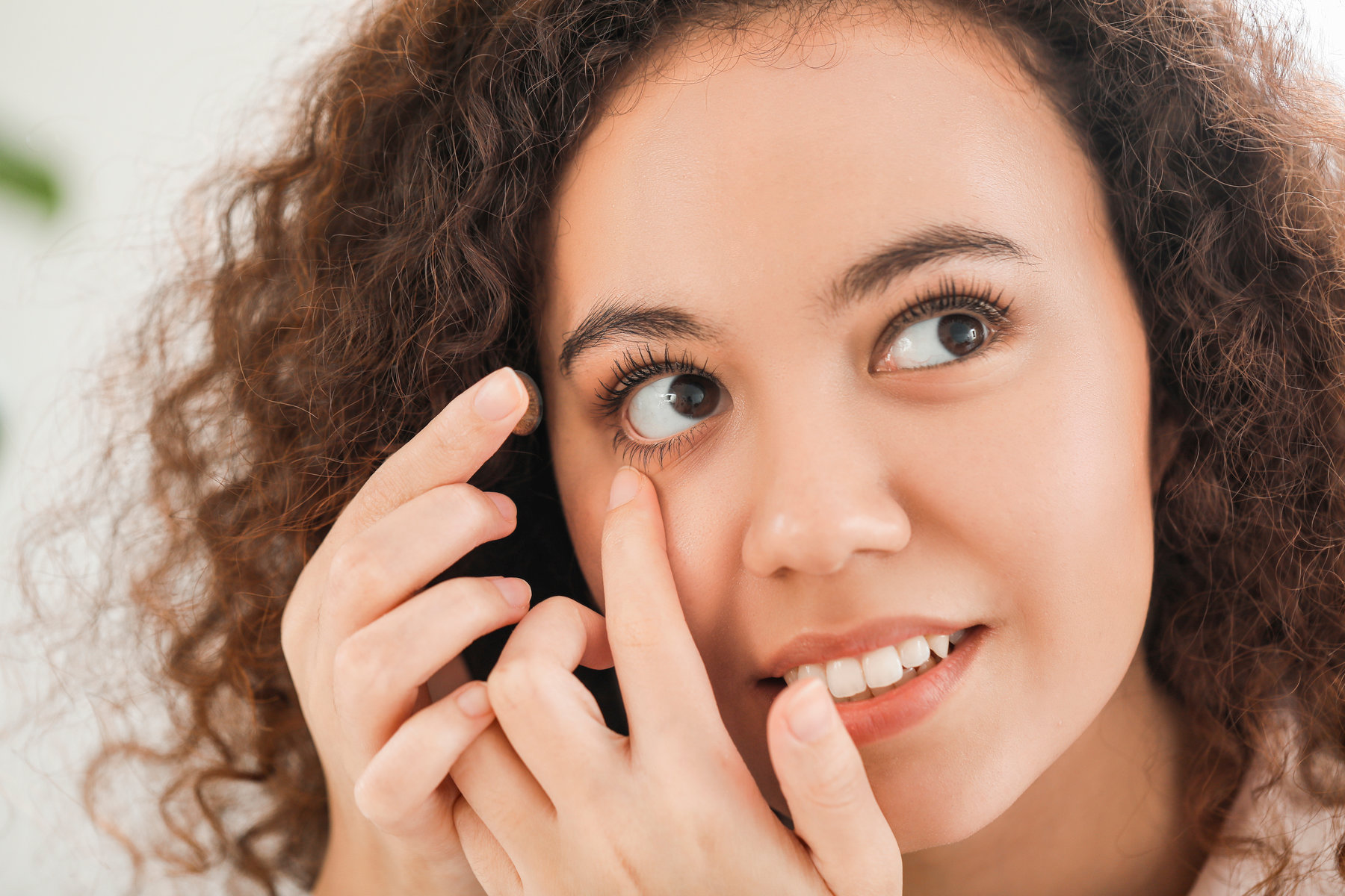 Young African-American woman putting in contact lenses at home